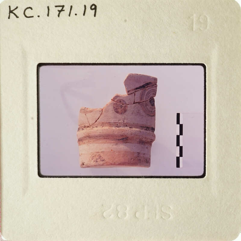 A photograph of an artifact, possibly a pottery shard with markings, on a white background.