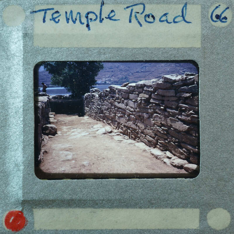 Stone wall with a dirt path and trees in the background.