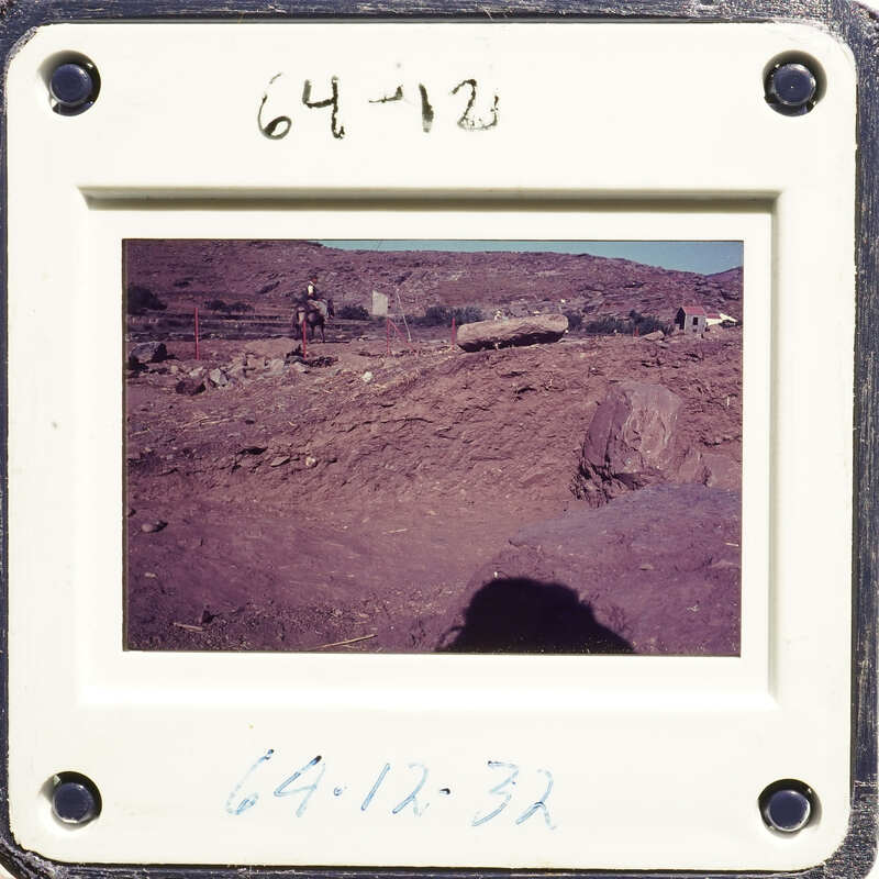 This is an old photograph showing a dirt road and rocky terrain with people standing nearby, possibly working on a construction site.