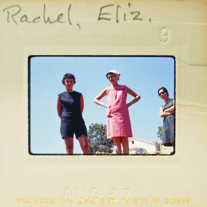 A vintage photo of three women standing together, with two wearing dresses and the third in a blouse and shorts.