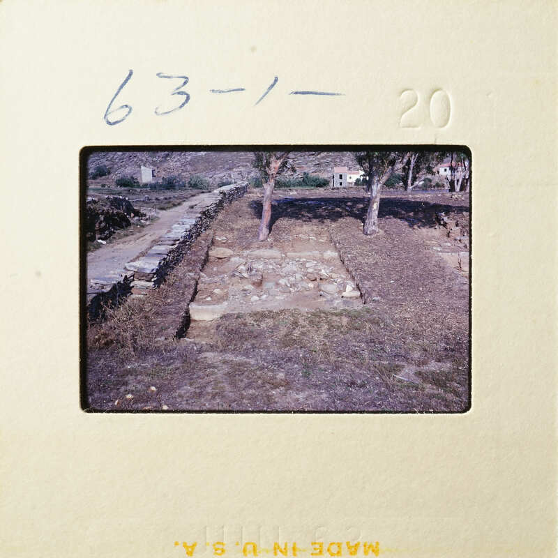 Ancient ruins with stone columns and walls, partially covered by dirt and vegetation.