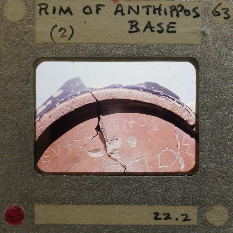 A photograph of an ancient artifact with Greek writing on it, displayed within a film strip frame.