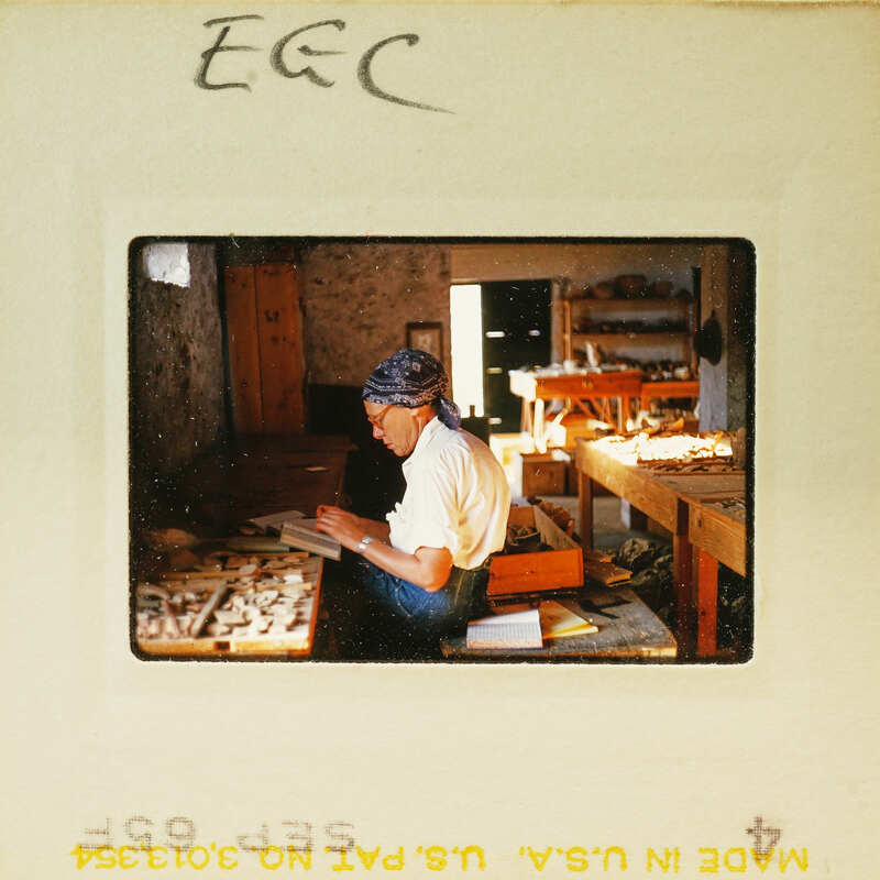 A woman sitting at a table with various items, possibly working on some craft or repair work, inside an old building.