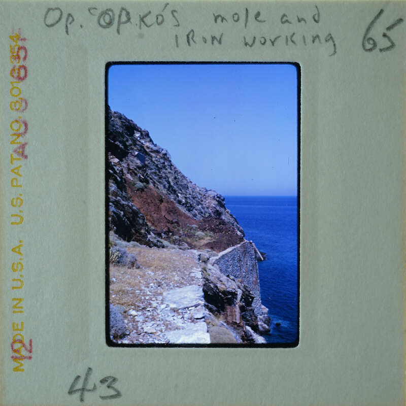 A vintage photograph of a coastal landscape with cliffs and the ocean, labeled "OP. SPIROS'S IRON WORKING".