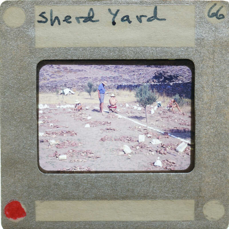 A slide of a yard with people, trees, and piles of pottery.