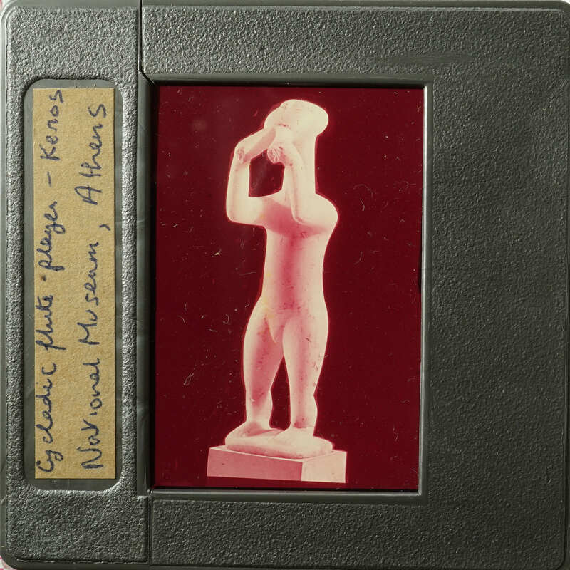 A photograph of an ancient Greek statue on display, taken from behind glass.