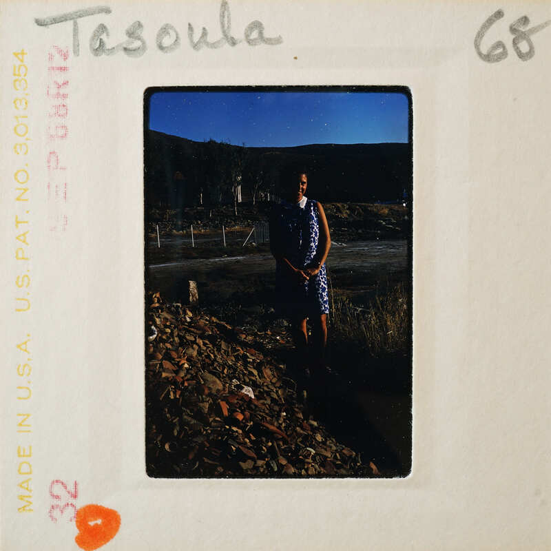 A vintage photo of a person standing on a rocky surface with mountains in the background.