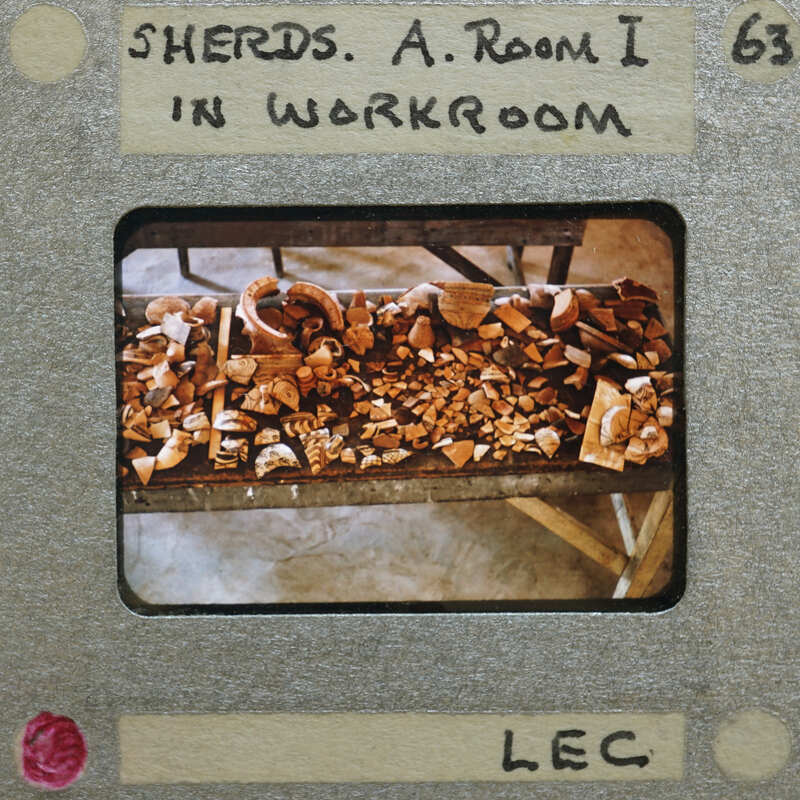 Old slide with a label and an image of a workbench with pottery shards on it.