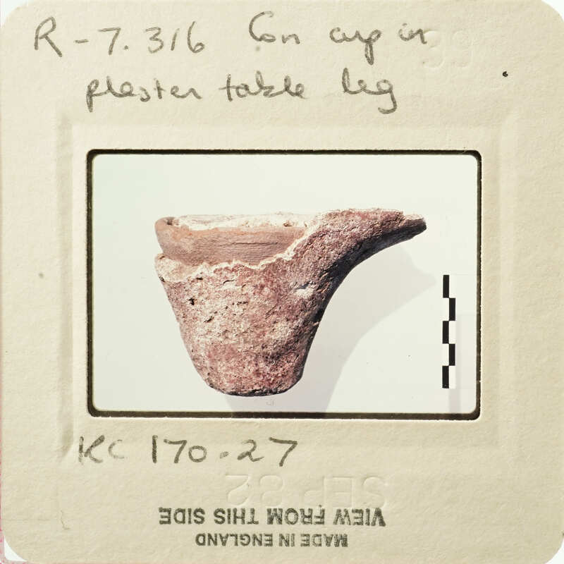 Ancient artifact, possibly a bowl or cup, with visible wear and tear, displayed on a white surface.
