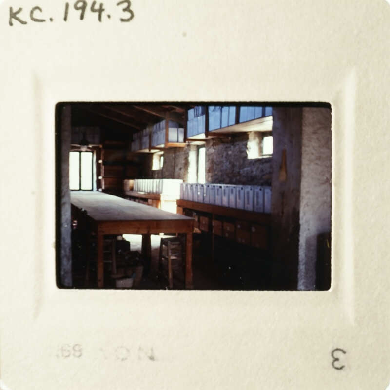 The photograph shows an empty room with long tables and benches, taken from a low angle.