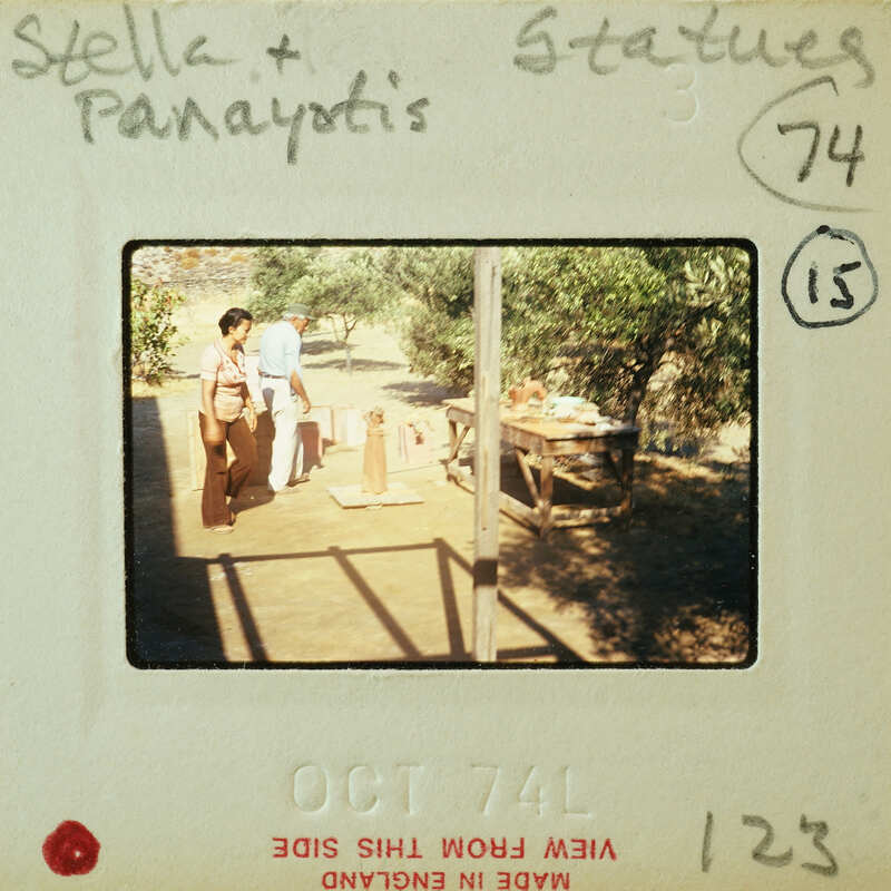 Two people standing near a wooden table with food and drinks on it, under an outdoor structure.