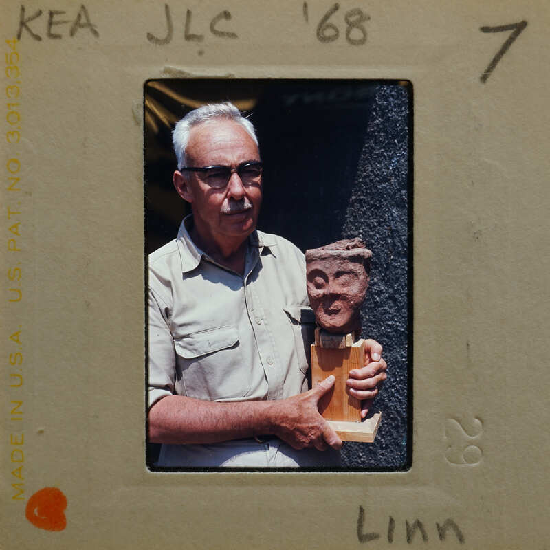 Man holding a terracotta figurine head (K1.458)mounted on wood.