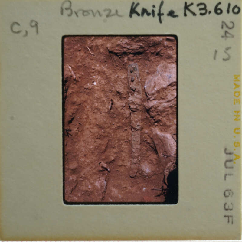 A close-up image of a bronze knife with an intricate handle, displayed on a card.