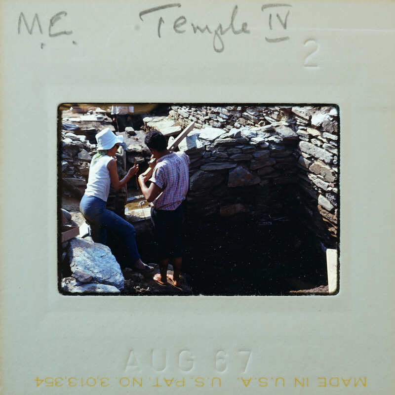 A vintage photo of two people working on a stone structure with handwritten notes.