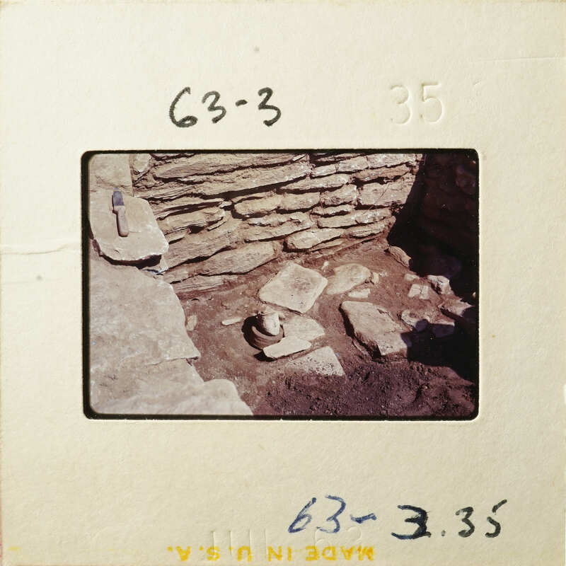 Old photograph showing an excavation site with stone ruins and a tool, possibly a chisel.