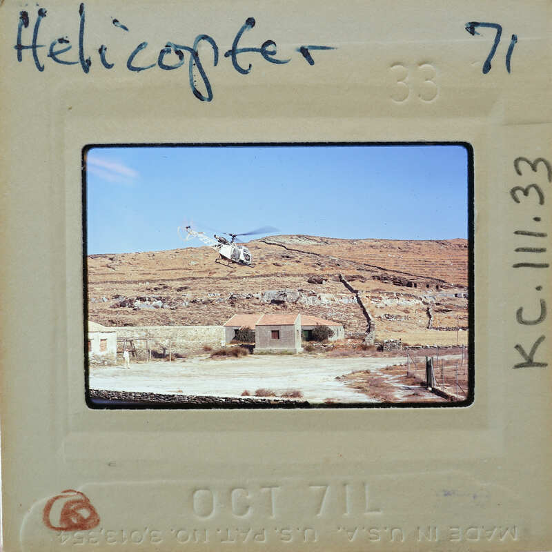 Helicopter flying over a hilly landscape with a small building.