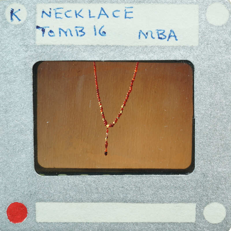 Red and gold necklace on a display stand with labels.