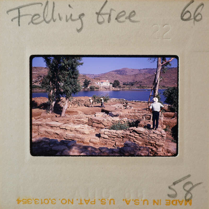 Man standing near a body of water with mountains and trees in the background.
