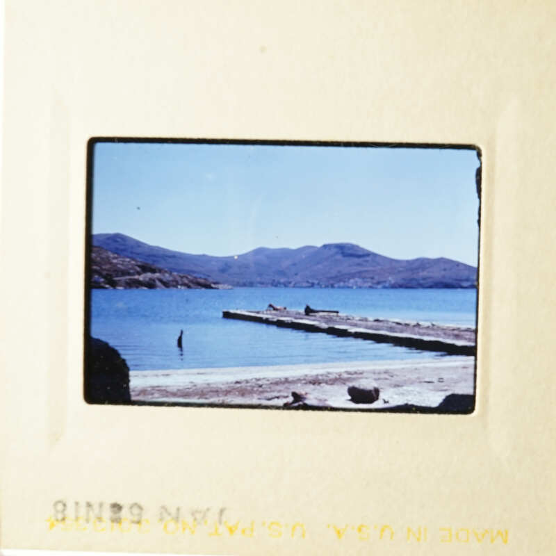 This photo shows a serene beach scene with a dock and mountains in the background.