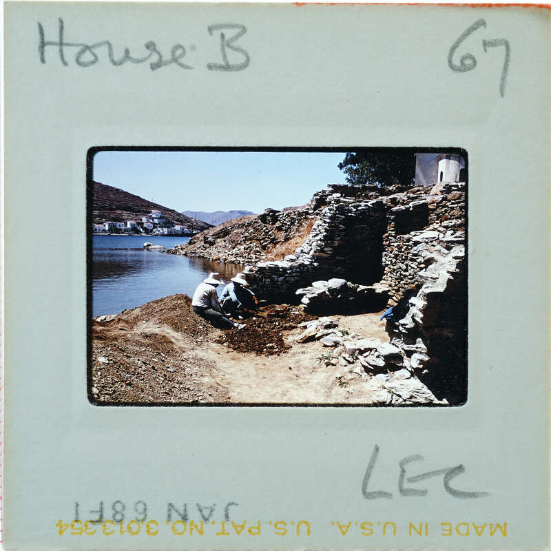 A black and white photo of a person working on a stone structure near water, with handwritten notes on the film strip.