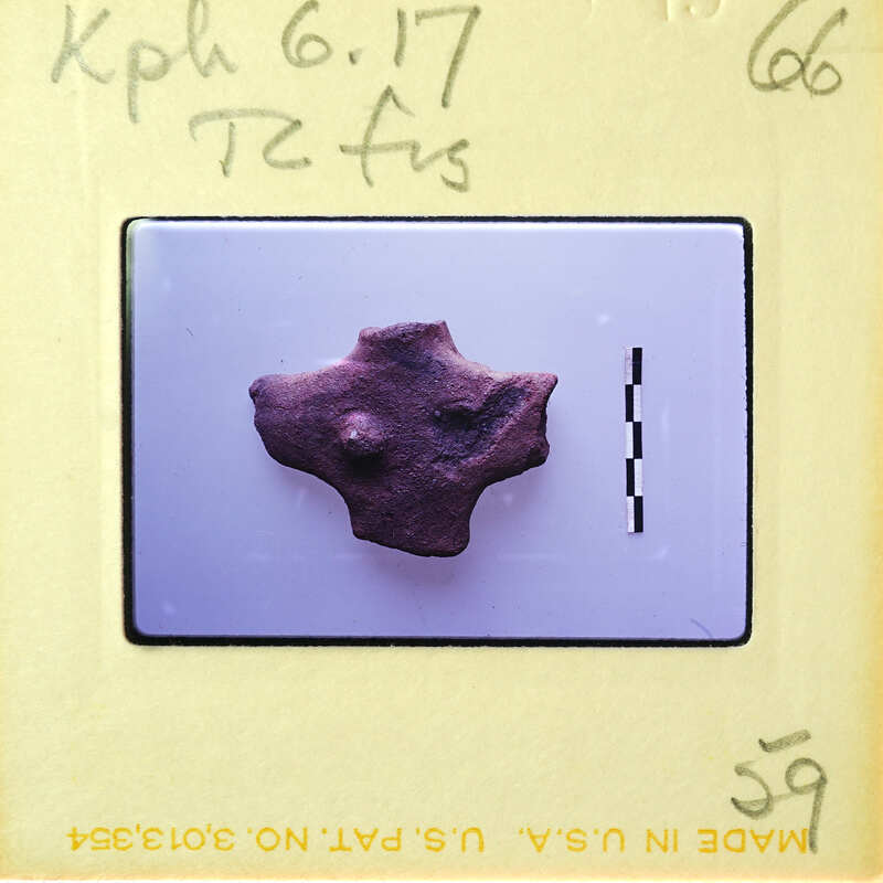 A small, irregularly shaped rock specimen on a white surface with measurements and annotations around it.