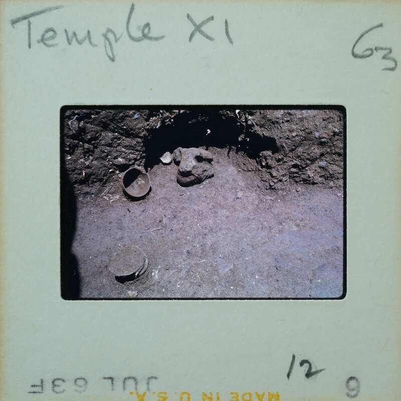 Stone wall with niche at bottom and pottery on the floor.