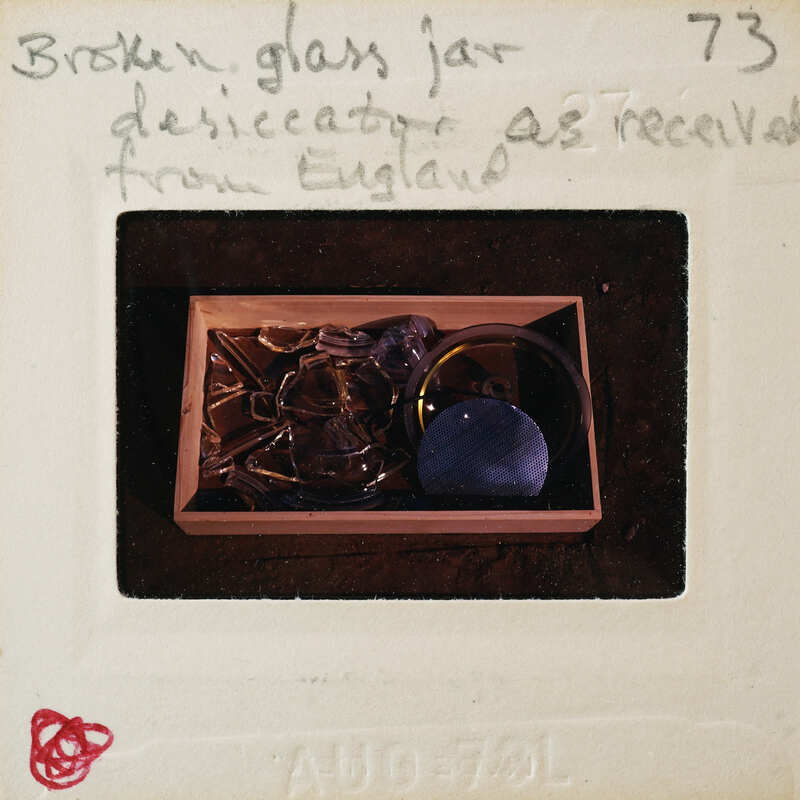 A broken glass jar in a box with a label indicating it was received from England.