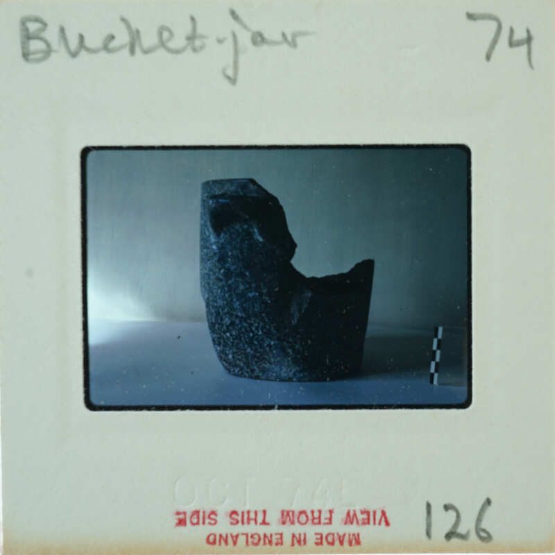 A photograph of a unique, dark-colored sculpture with an abstract shape and texture, displayed on a white surface.