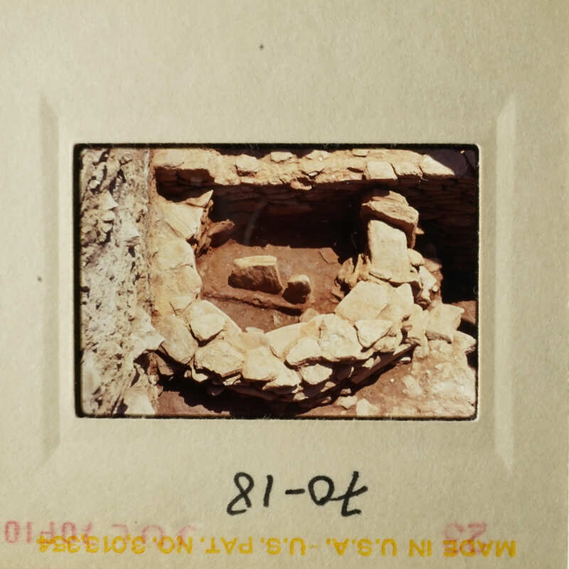 This is an old photograph showing a stone structure, possibly an ancient burial site or ruins, with a small cave-like entrance and a few stones scattered around.