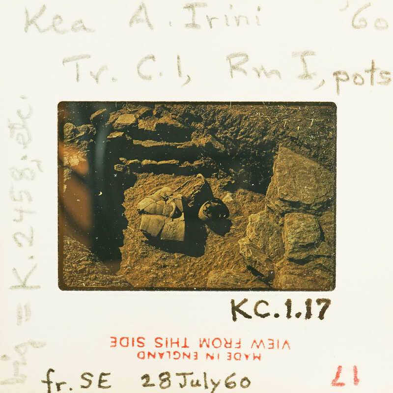 A vintage black and white photograph of a cave with human-like figures, possibly early humans or statues, on the ground.