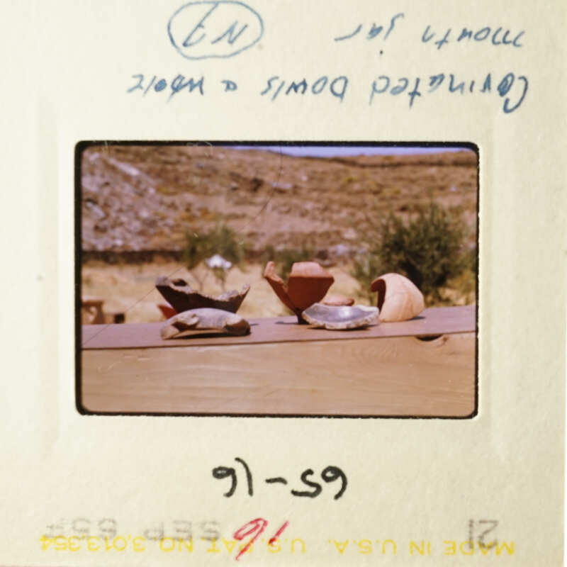 A photograph of a wooden table with various items on it, including a cup and a bowl, set against a backdrop of a rural landscape.