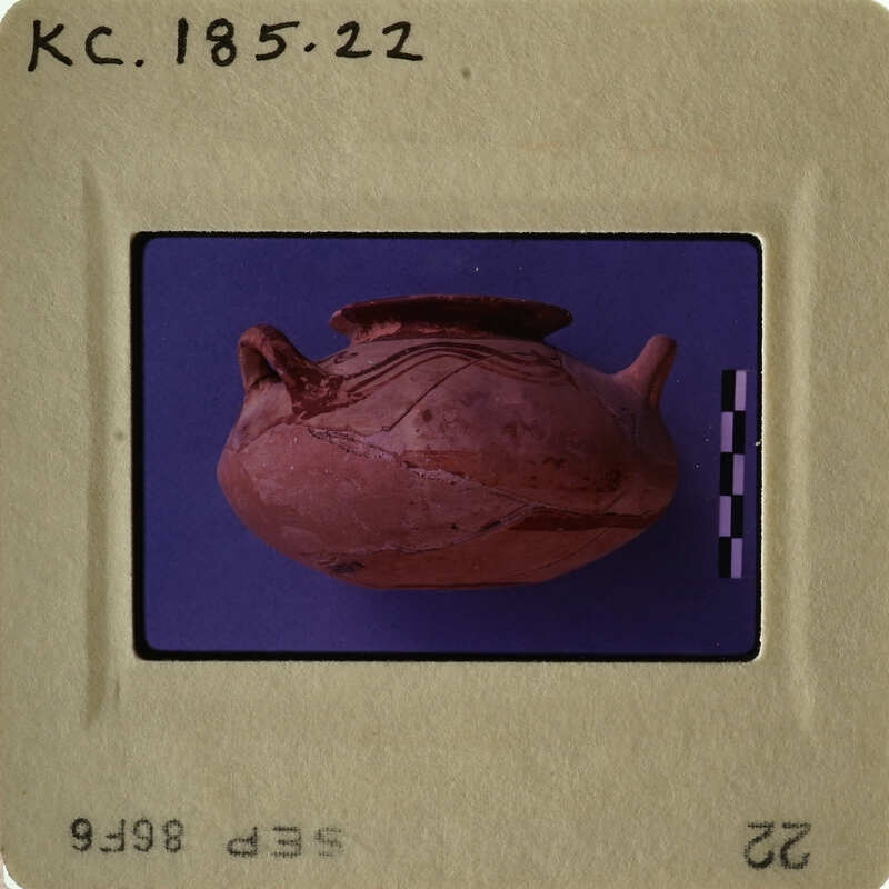 Ancient clay pot with handle and spout, photographed on a purple background.