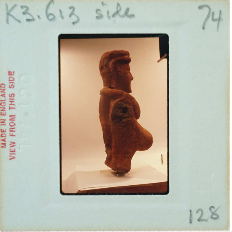 A photograph of an ancient clay figurine with a prominent belly, displayed on a stand.