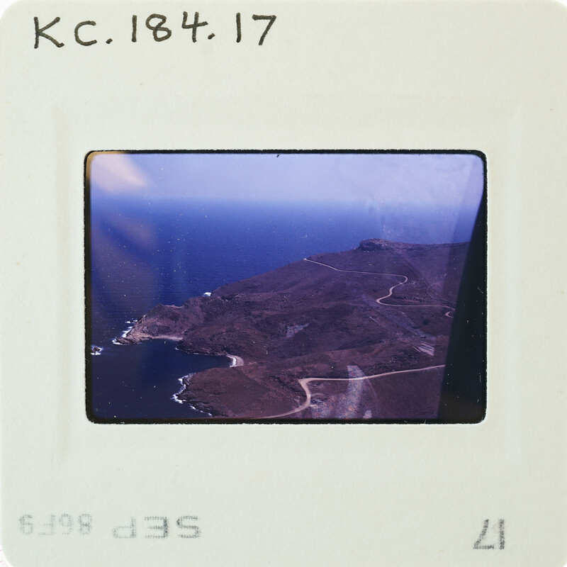 Aerial photograph of a coastal landscape with an ocean, land, and roadway.