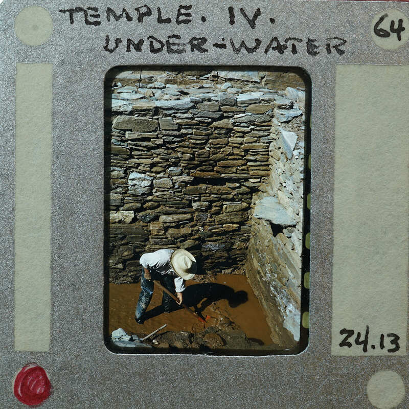 A man working on a stone structure underwater, with a dated film strip border.