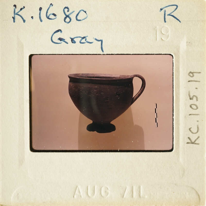 The image shows an antique cup with a handle, photographed against a light background.