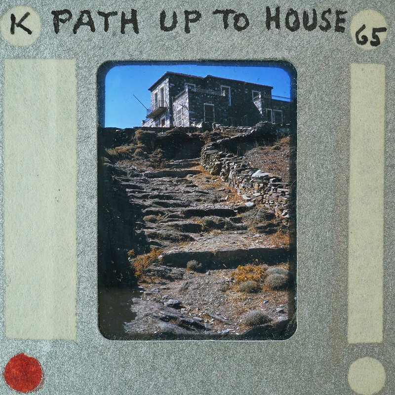 A photograph of a stone house with a path leading up to it, set against a mountainous landscape.