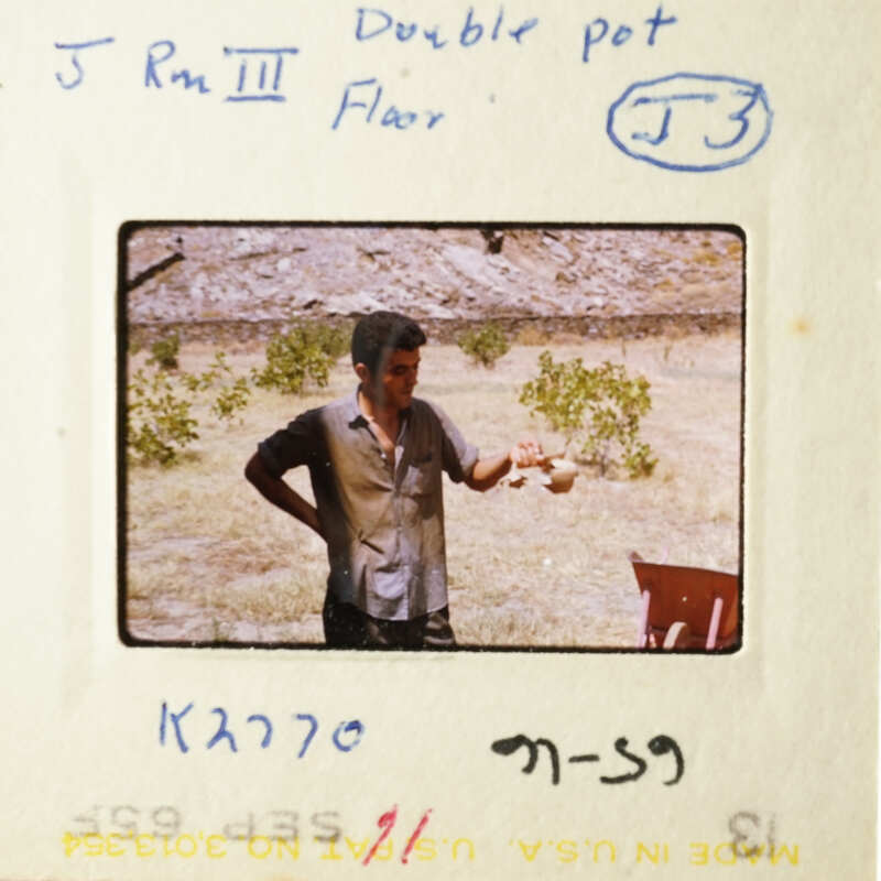 A man holding a cup in front of a tree and a building.