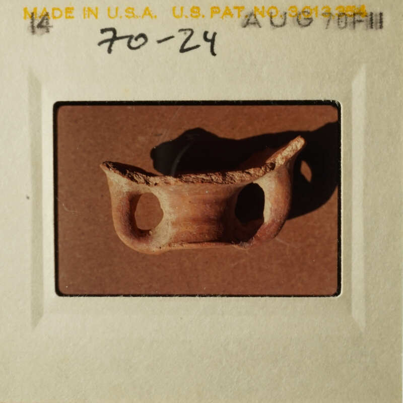 The image shows a small, handmade clay pot with a handle on top, placed on a table.