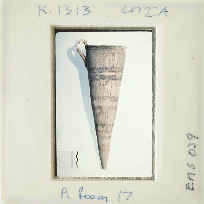 Ancient artifact on display, possibly a clay pottery piece with handle and markings.