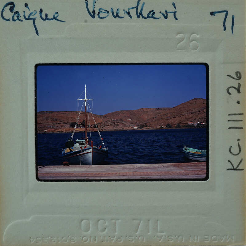 Photograph of a boat docked at a pier with mountains in the background.