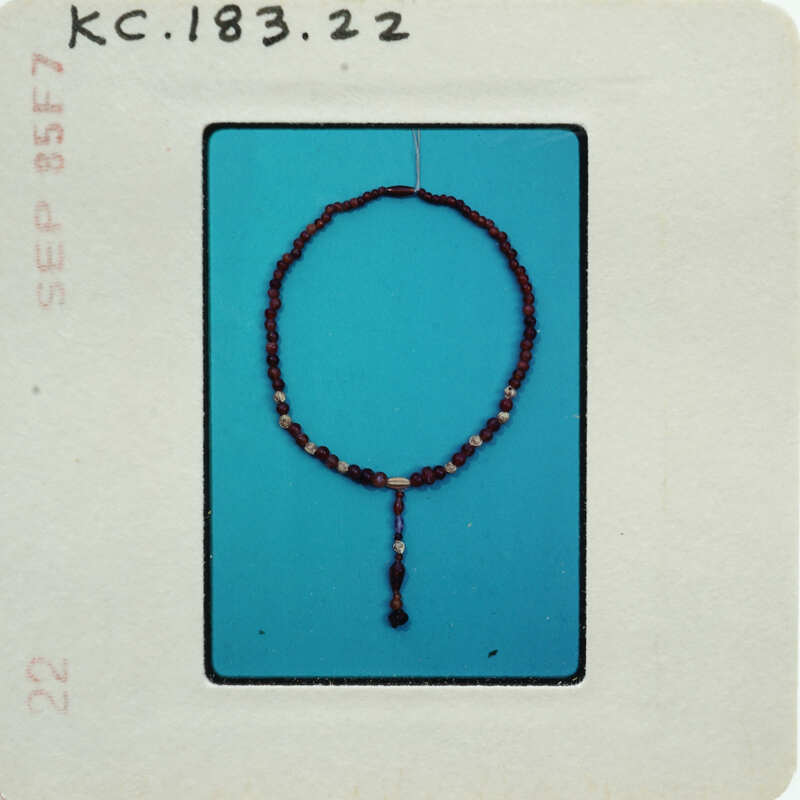 A bead necklace with a tassel, photographed against a blue background and placed on a white card.