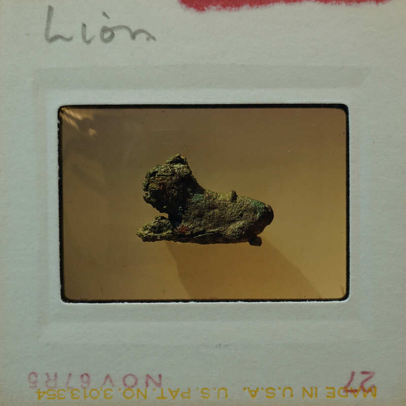 Small bronze statue of lion from the side in poor condition.