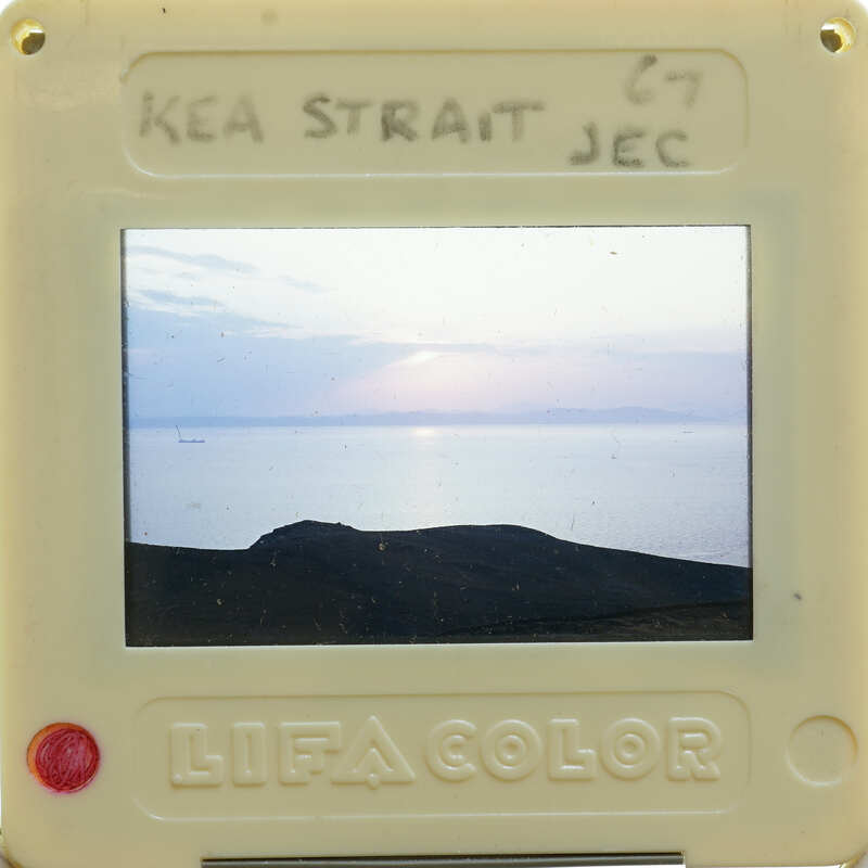 A small camera displaying a photo of a sunset over water with mountains in the background.