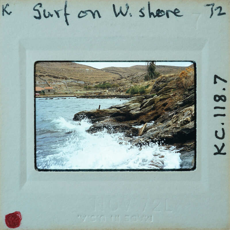 A rocky shoreline with crashing waves and distant mountains.