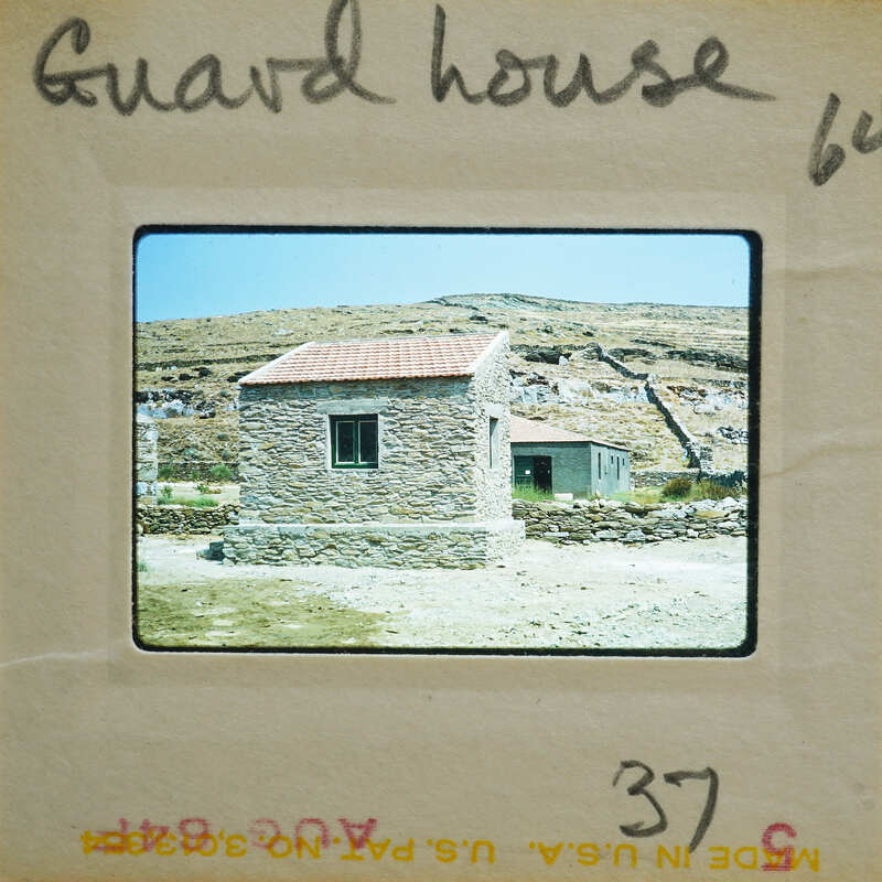 Old stone guard house with a red roof, set against a mountainous landscape.
