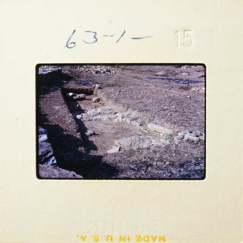 Ancient ruins with stone walls and foundations partially uncovered on a dirt field.