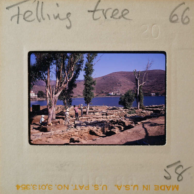 Ancient ruins near a body of water with trees and mountains in the background.