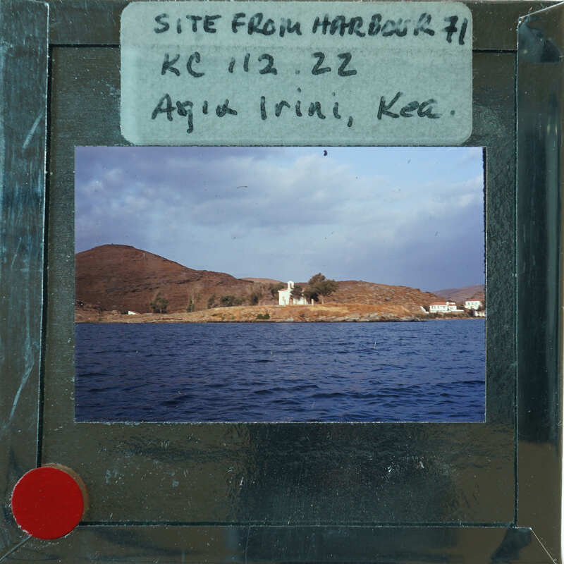 A view of a coastal town with buildings, a churche and mountains from the water.