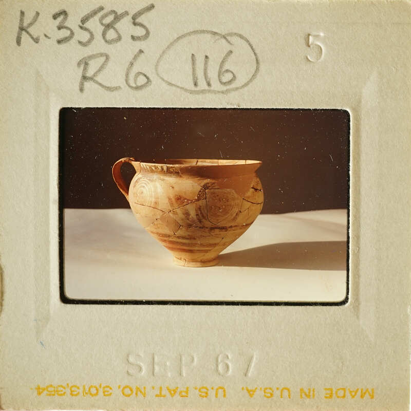 Ancient-looking ceramic vase with visible cracks and imperfections, photographed on a light surface.